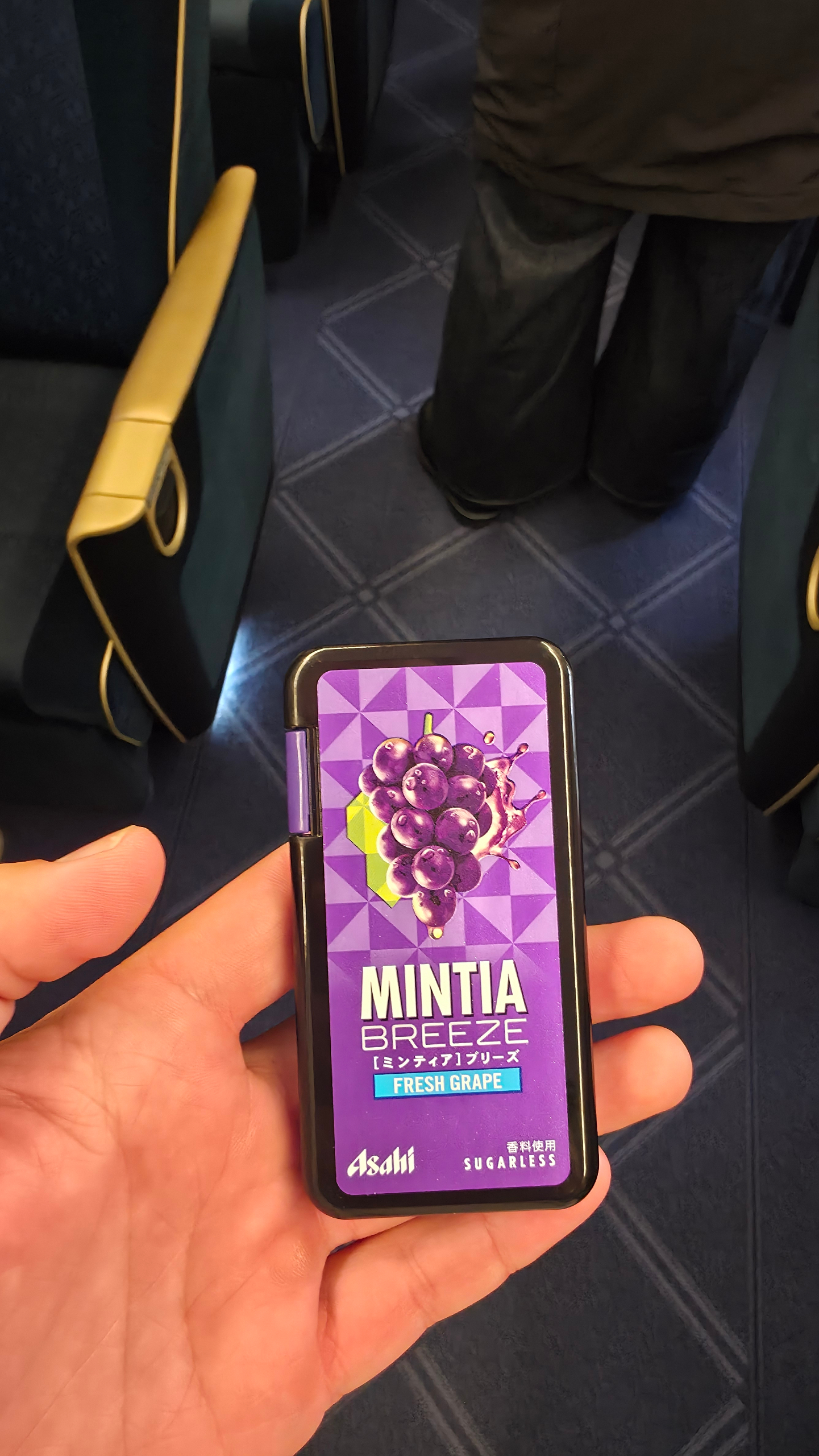 Original Mintia Breeze candy package design with white text and a purple grape illustration on a geometric purple background. logo featuring purple, black, blue colours