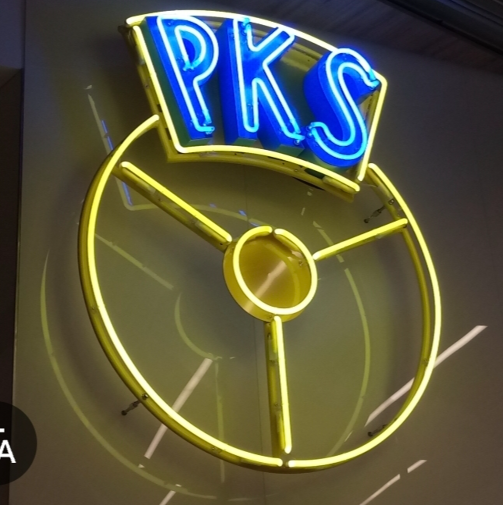 Original blue text 'PKS' above a large yellow circular steering-wheel icon with three spokes and a central oval logo featuring yellow, blue, white colours