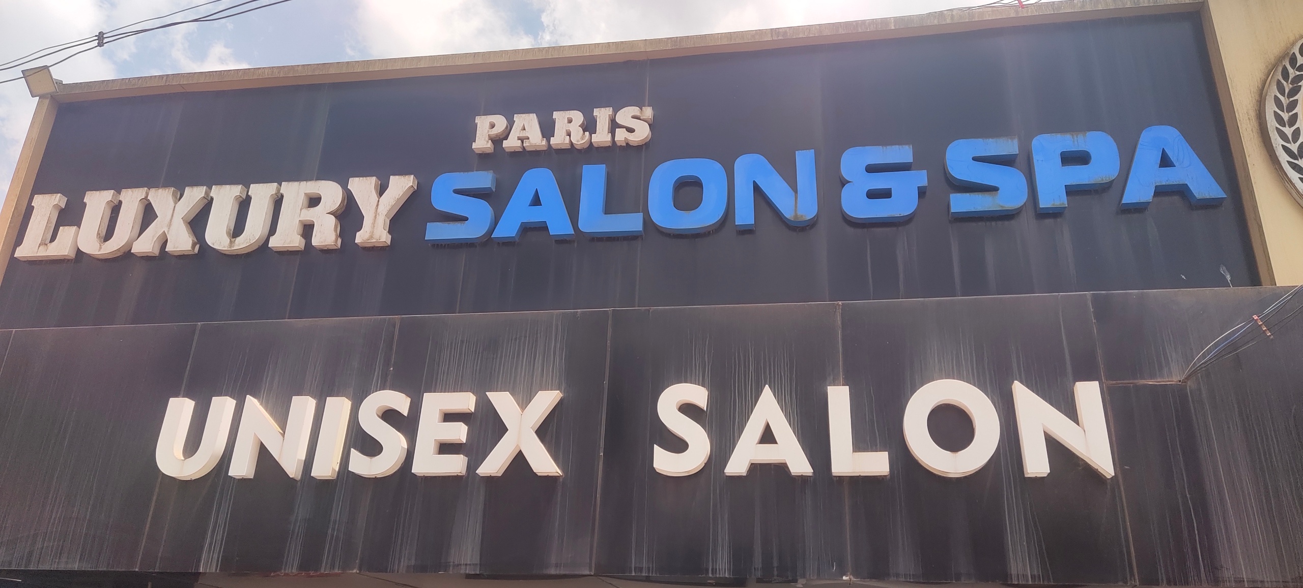 Original storefront sign text reading 'PARIS LUXURY SALON & SPA' and 'UNISEX SALON' in large block letters on a dark background logo featuring black, white, blue colours