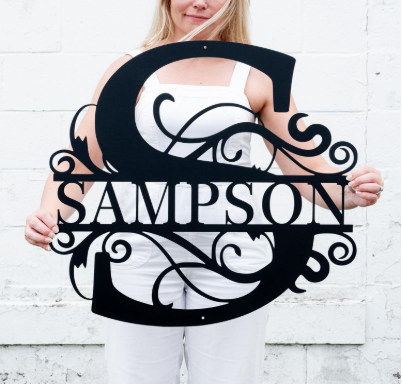 Original black decorative letter S sign with the name 'SAMPSON' across the center in bold capitals and ornamental scrollwork inside the S shape logo featuring white, black, skin colours