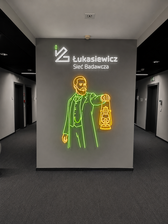 Original white text logo 'Łukasiewicz Sieć Badawcza' above a neon green and yellow line-art figure of a bearded man in a suit holding a lantern logo featuring gray, black, neon green, neon yellow colours