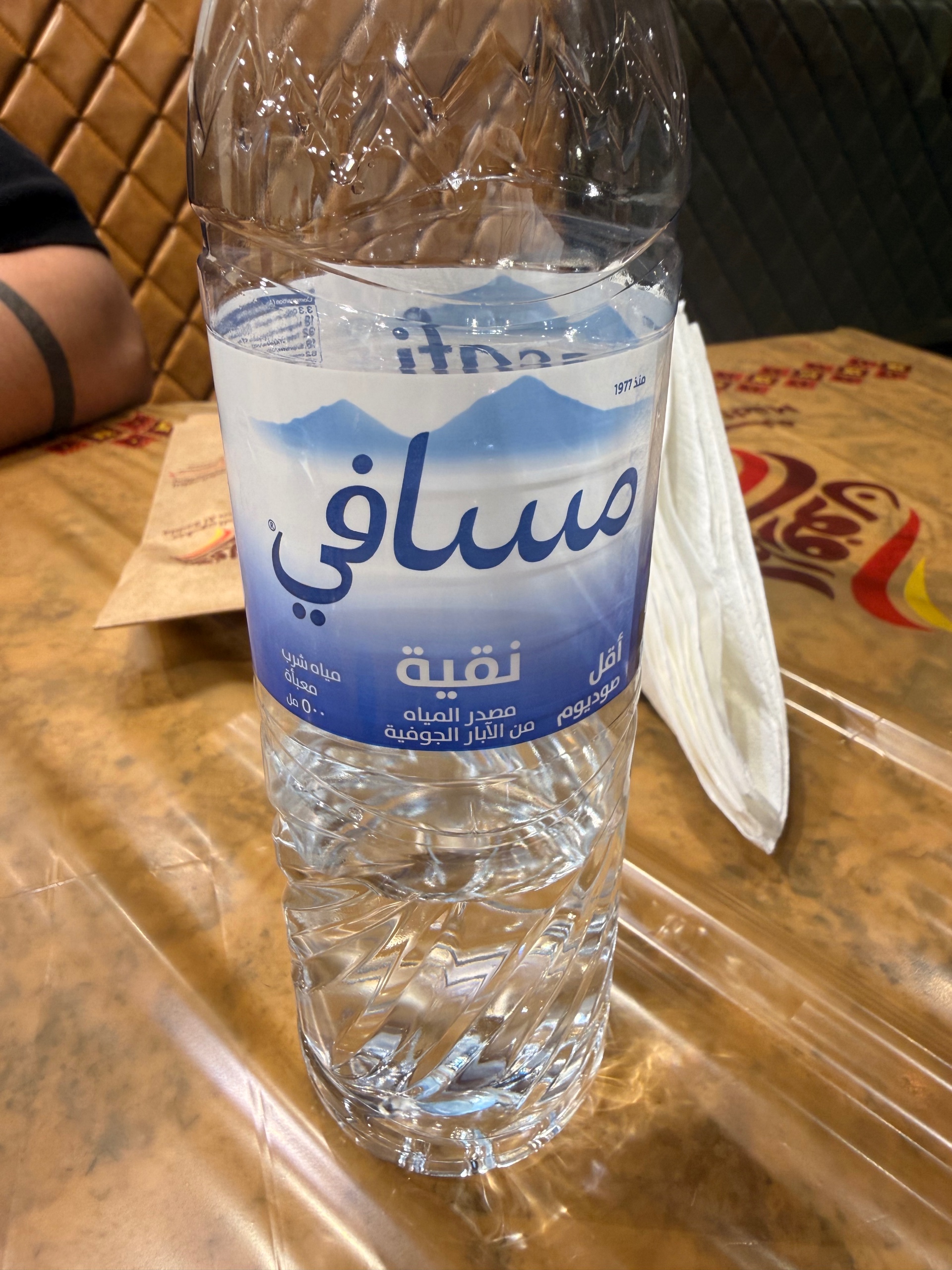 Original blue and white water bottle label with Arabic text and stylized blue mountain graphic logo featuring blue, white, brown colours